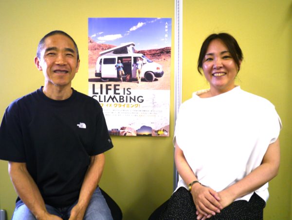 画像:ポスターの前　笑顔の小林さんと松田　ウエストまでの2ショット